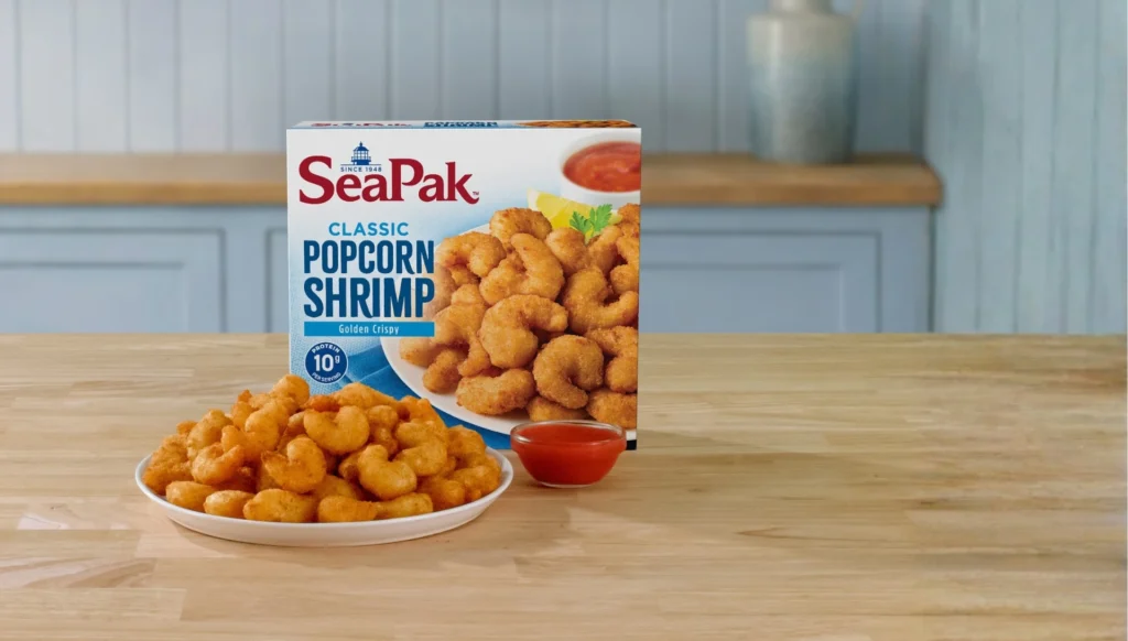 Plate of classic popcorn shrimp on a kitchen counter with the product box displayed behind it.